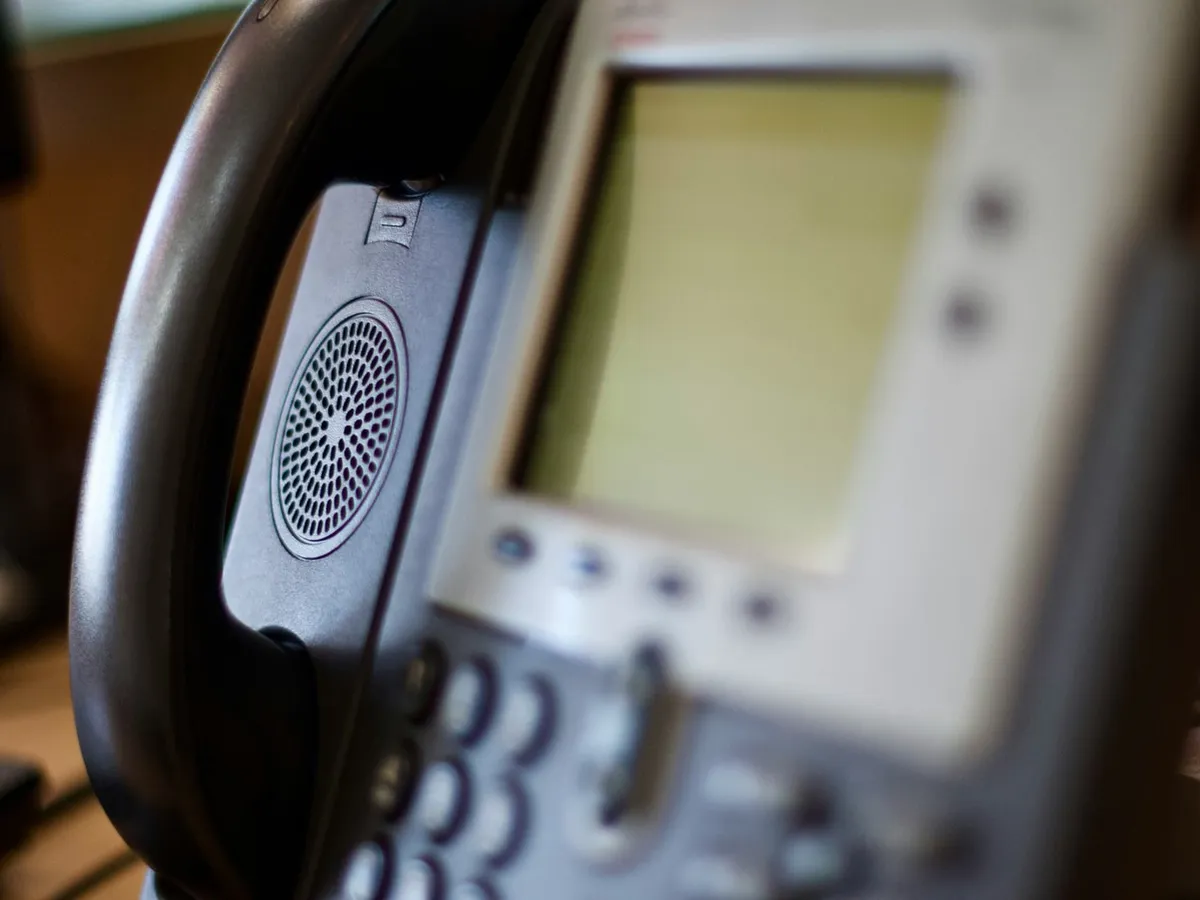 A desk telephone, close up, with the handset resting on its base
