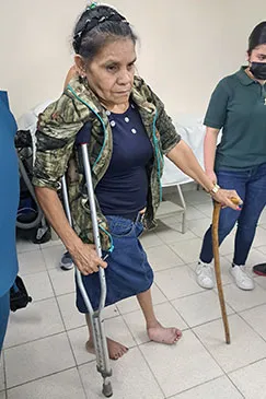 A patient walking with a crutch and a cane in a clinic corridor