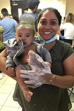 A smiling member of the team holding a baby wrapped in a towel, with a small cast on one leg
