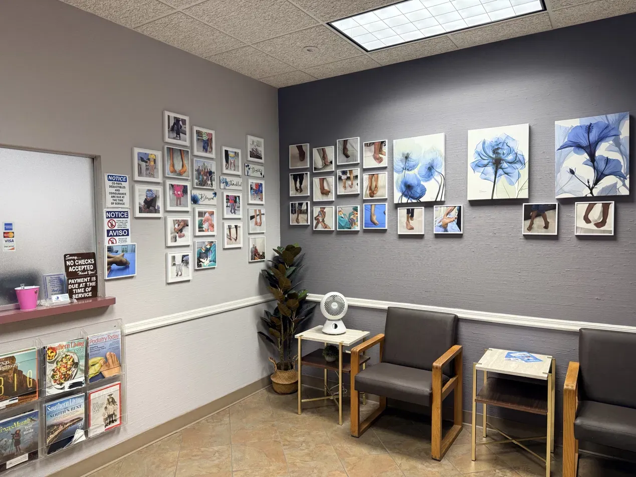 The Total Podiatry waiting room: chairs and side tables against a gray wall, with framed photographs and blue flower prints, a magazine rack, and the reception window